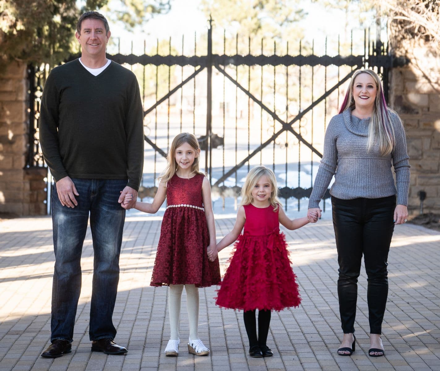 Dr. Tyler Karlin with his wife and their two daughters, holding hands in front of an iron gate